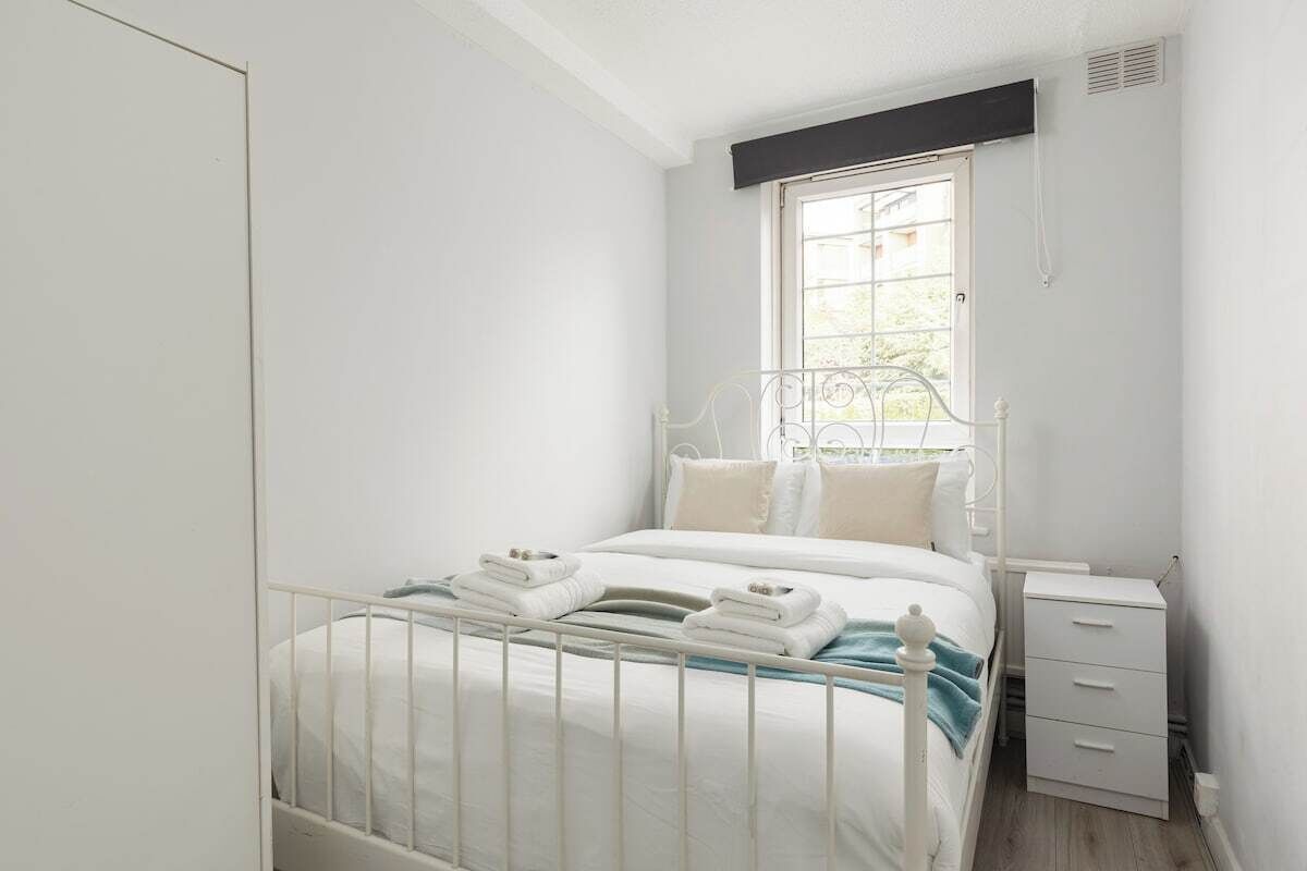 Een slaapkamer met een bed, nachtkastje en raam.
