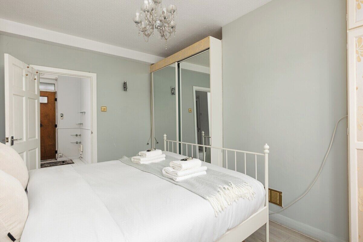 A bedroom with a bed, a mirror, and a door leading to another room.