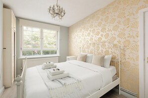 A bedroom with a bed, a chandelier, a window, and a patterned wall. - New! Lovely 3BR w/Garden | 6 Mins to Canada Water (Greater London)