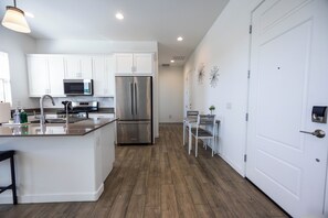 A modern kitchen with white cabinets, stainless steel appliances, and a wooden floor.