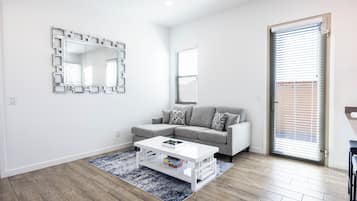 Een moderne woonkamer met een grijze bank, een witte salontafel en een tapijt met dessin.