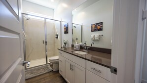 A modern bathroom with a glass-enclosed shower, a toilet, a sink, and a large mirror. - The Villa Suite @ Gilbert | Garage + Community Pool (Gilbert)
