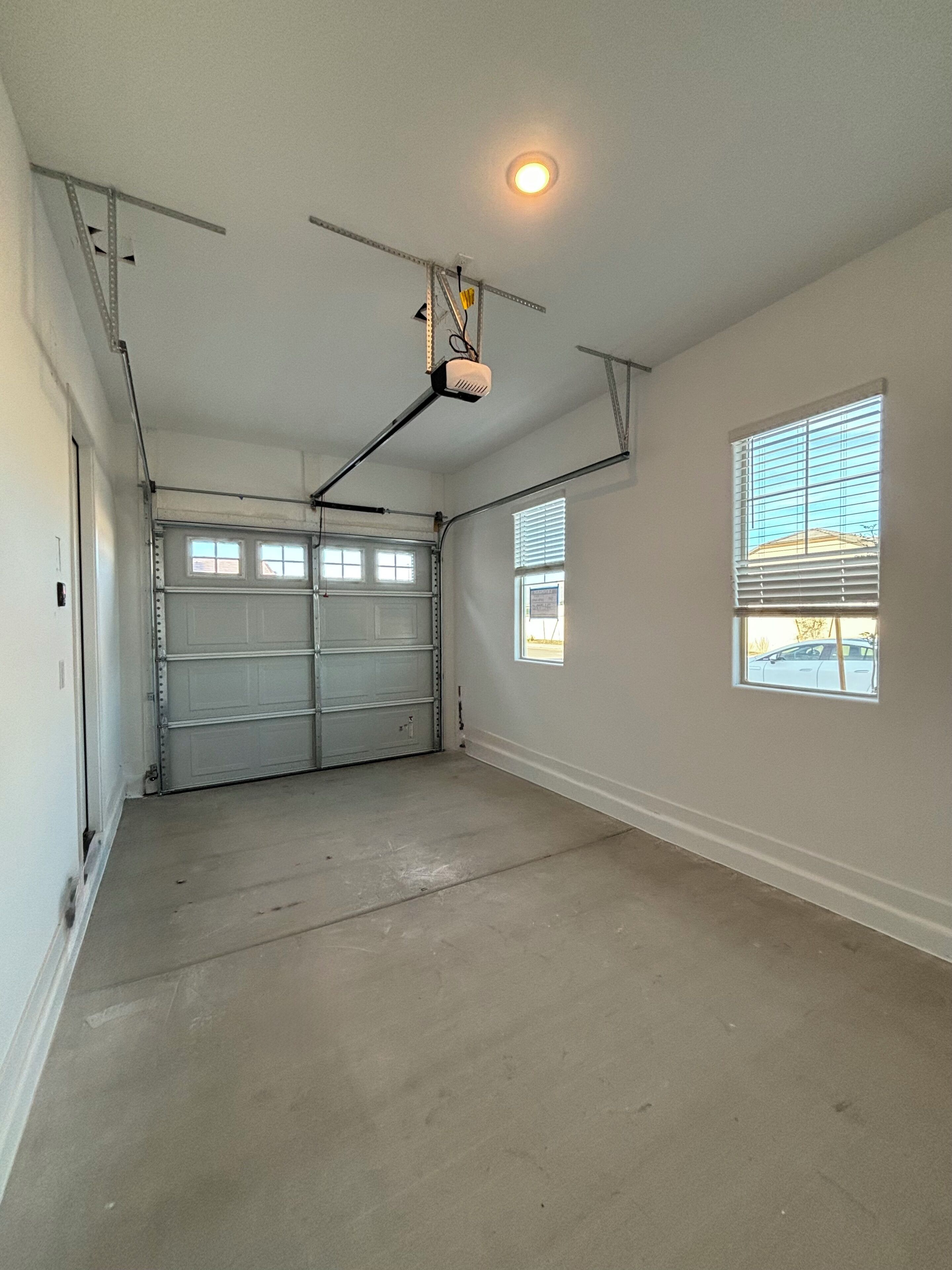 A garage with two double doors, a ceiling-mounted light fixture, and two windows with blinds.
