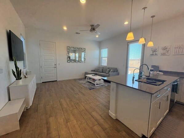 A modern kitchen with a central island, a dining area with a sofa, and a large window providing natural light.