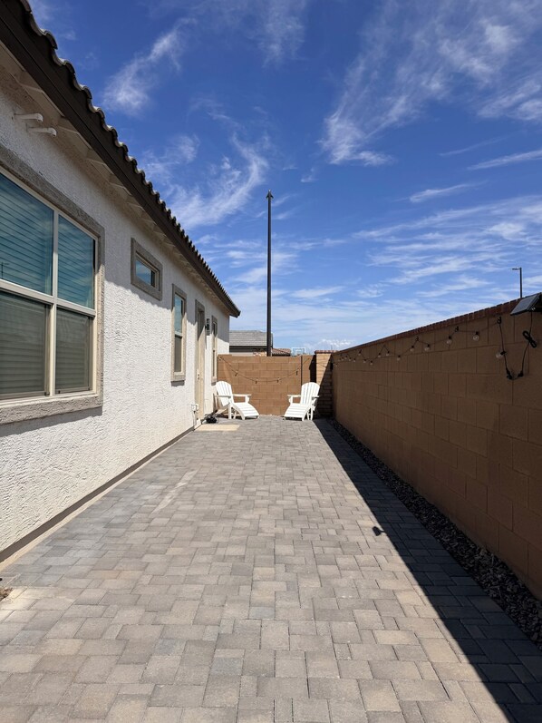 A patio area with two white chairs, a brick wall, and a clear blue sky.