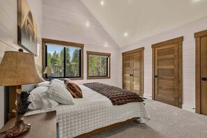 Une chambre à coucher avec un lit, une lampe, un tableau et une vue sur les arbres à travers les fenêtres.