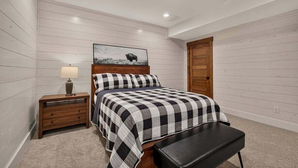 A bedroom with a bed, a nightstand, a bench, and a door. - Pine and Sky Lodge+WiFi+AC+Hotub+30Min2Yellowstone (Island Park)