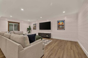 Un salon moderne avec un canapé d’angle, un téléviseur à écran plat fixé au mur et un plancher en bois.