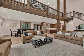 A spacious living area with a high ceiling and a mezzanine level, featuring a dining area and a kitchen. - Pine and Sky Lodge+WiFi+AC+Hotub+30Min2Yellowstone (Island Park)