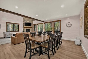A spacious living area with a large wooden dining table surrounded by chairs, a fireplace, and a television mounted on the wall. - Pine and Sky Lodge+WiFi+AC+Hotub+30Min2Yellowstone (Island Park)