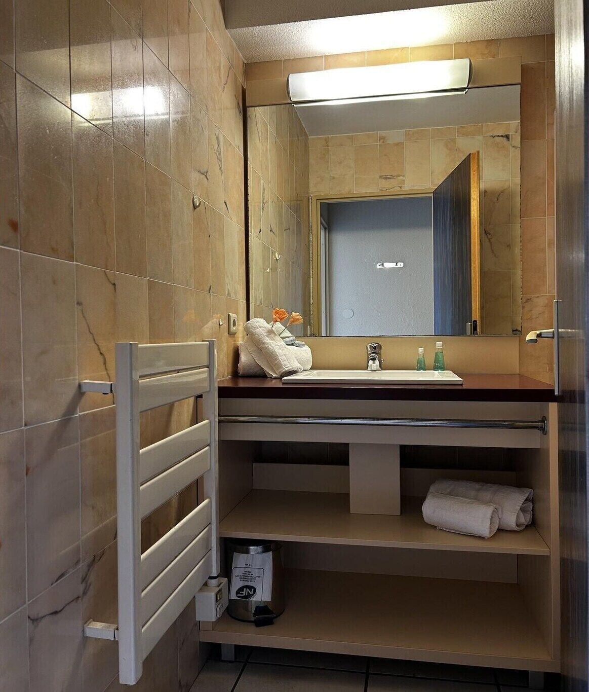 Ein Badezimmer mit Spiegel, Waschbecken, Handtuchhalter und Mülleimer.