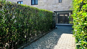 A paved pathway flanked by neatly trimmed hedges leading to a building with a modern architectural style. - Corba Luxury Lake View Apartment (Canobbio)