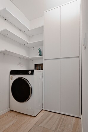Ein Waschraum mit Waschmaschine, Trockner und einem hohen, weißen Kleiderschrank.