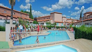 Área de piscina cercada, com palmeiras e edifícios com telhados de barro.
