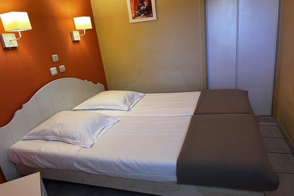 A double bed with white and brown bedding, two wall-mounted lamps, a small statue, and a closed door.