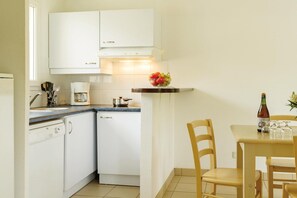 A compact kitchen with white cabinets, a coffee maker, and a fruit bowl on the counter.