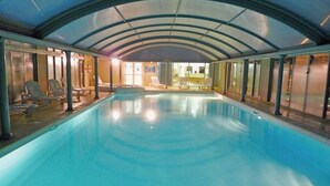Une piscine intérieure dotée d’un plafond incurvé et de chaises longues disposées le long des parois.