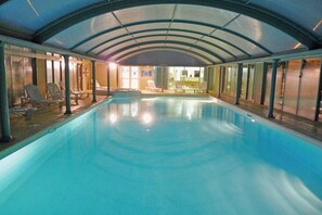 An indoor swimming pool with a curved ceiling and lounge chairs along the sides.