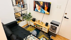 A living room with a black sofa, a TV mounted on the wall, a small white cabinet, and a decorative rug.
