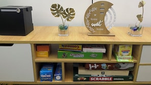 A wooden desk with a black speaker, two glass vases with artificial plants, a wooden calendar, and a small glass container with decorative items.