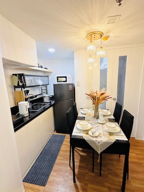 A compact kitchen with a black refrigerator, a microwave, and a stove. There is a dining table set with plates, glasses, and a vase with dried flowers.