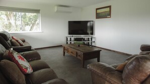 A living room with a large flat-screen TV, leather sofas, a coffee table, and a painting on the wall.