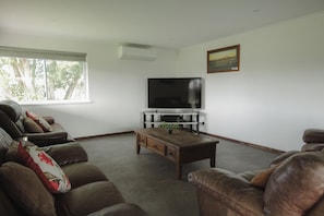 A living room with a large flat-screen TV, leather sofas, a coffee table, and a painting on the wall.