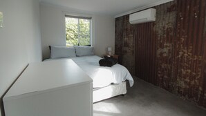A bedroom with a bed, a bedside table, a lamp, and a window.