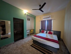 Un dormitorio con cama, escritorio, silla, ventilador de techo y aire acondicionado.