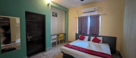 A bedroom with a bed, a desk, a chair, a ceiling fan, and an air conditioning unit.