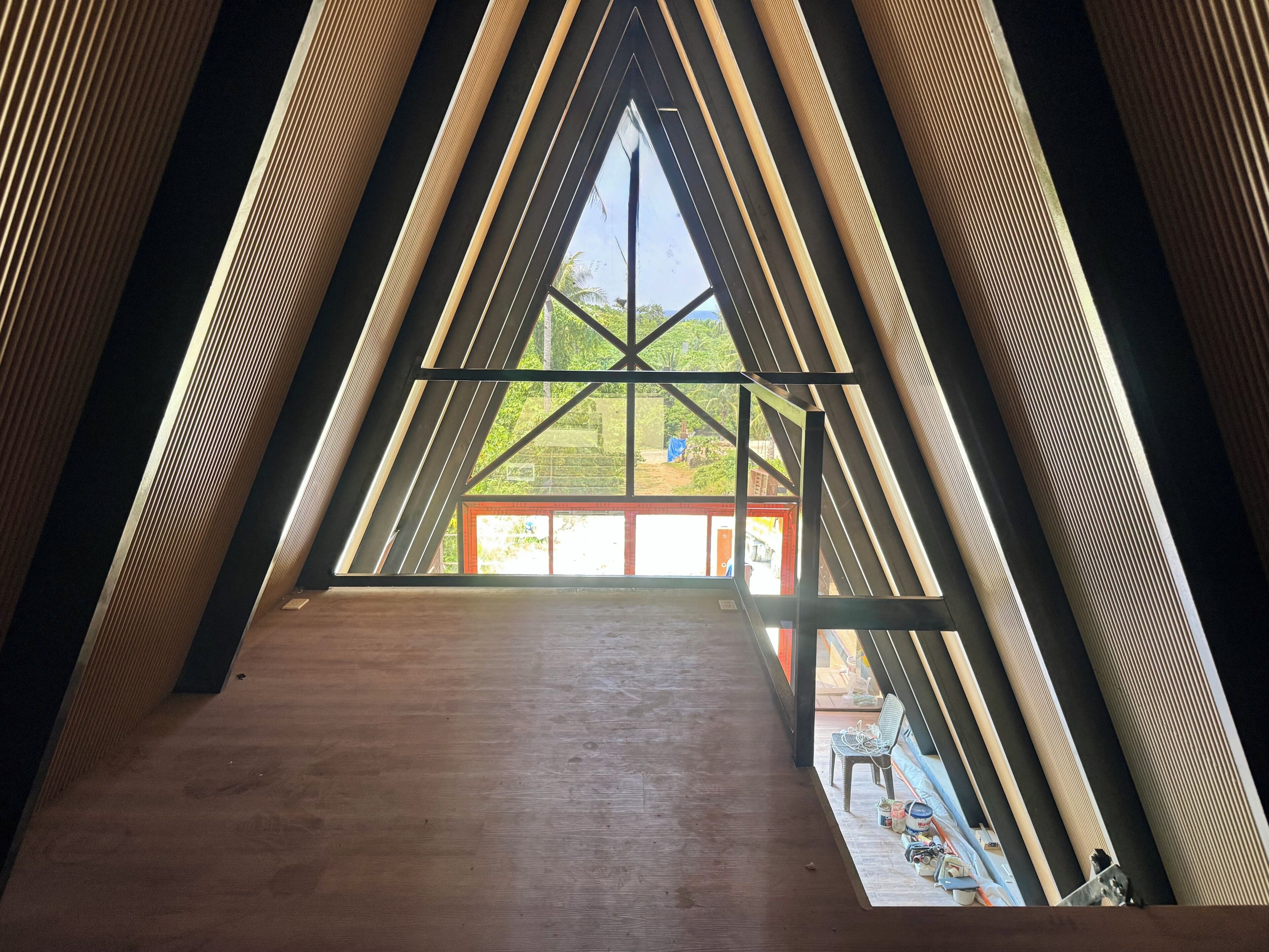 Une pièce triangulaire avec un plancher en bois et une grande fenêtre au fond.