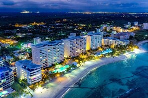 A coastal hotel with multiple high-rise buildings, a beachfront, and a swimming pool. - Beachfront 6th Fl | Amazing View | Full Kitchen (Juan Dolio)