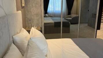 A modern hotel room with a large bed, a bedside table, and a mirror reflecting the room.