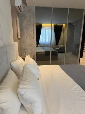 A modern hotel room with a large bed, a bedside table, and a mirror reflecting the room. - Fron Hotel (Pristina)
