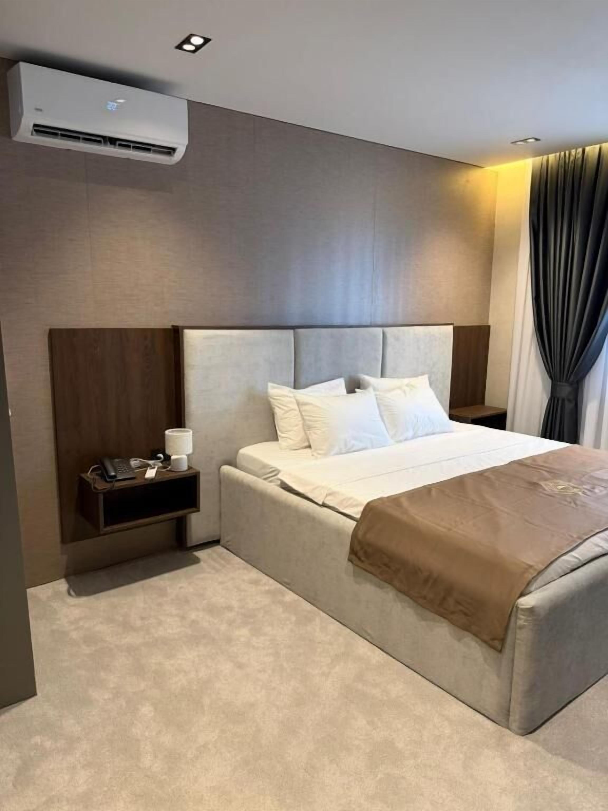 Una habitación de hotel con cama, mesita de noche y un equipo de aire acondicionado.