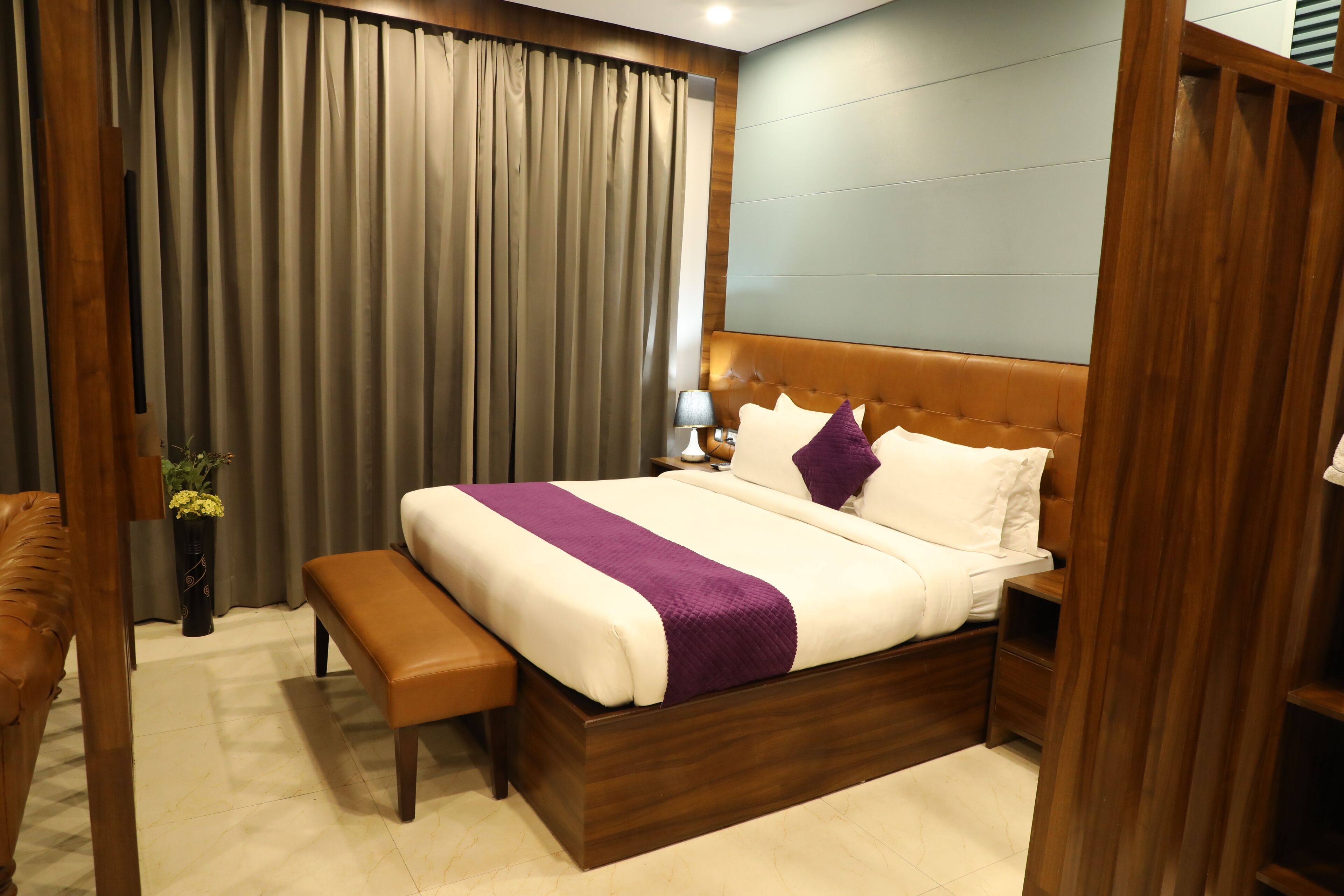 Una habitación de hotel con cama, reposabajares, mesita de noche, lámpara y planta en maceta.