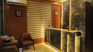 Un área de recepción con un muro de listones de madera, una mesa de recepción con detalles de mármol, una silla y una pequeña mesa con un jarrón de flores.