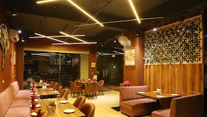 Interior de restaurante con paneles de madera, iluminación moderna y diversas opciones de asientos, incluyendo mesas y cabinas.
