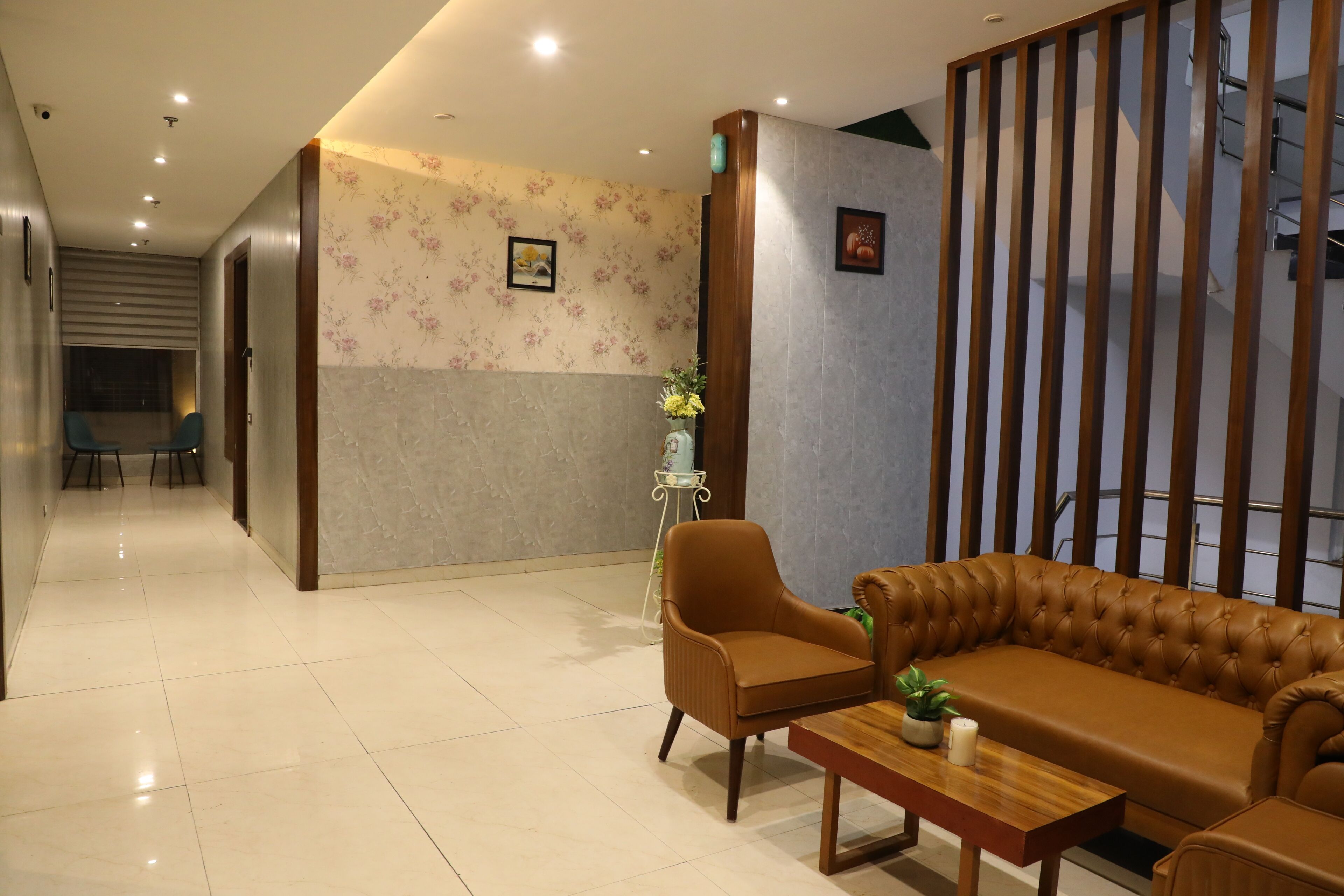 A modern hotel lobby with a sofa, armchair, and a small table with a plant and candle.