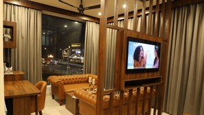 Una sala de estar moderna con televisión, sofá de cuero, mesa de centro de madera y vistas a un paisaje urbano nocturno.