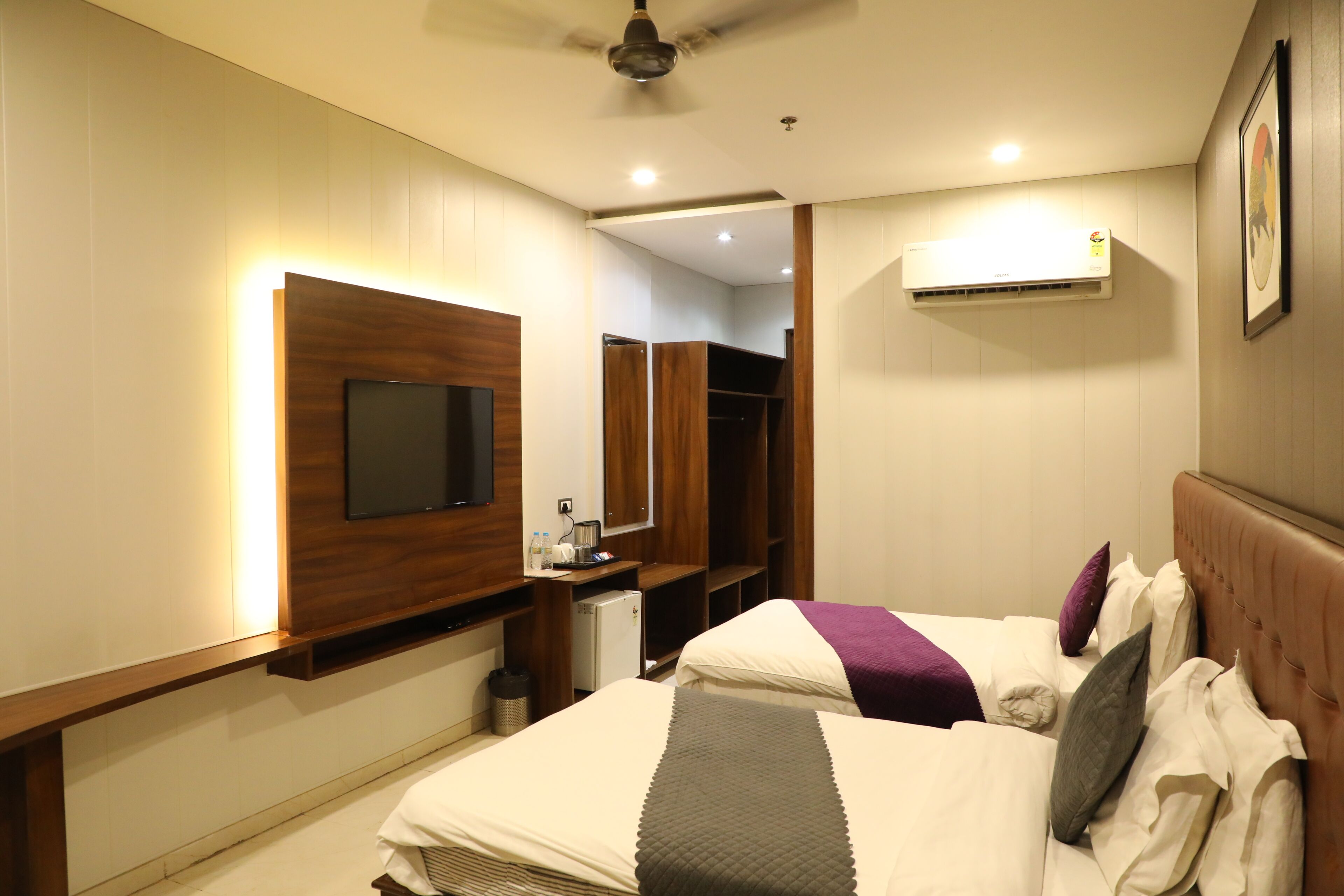 A hotel room with a bed, a TV mounted on the wall, a wardrobe, and an air conditioning unit.
