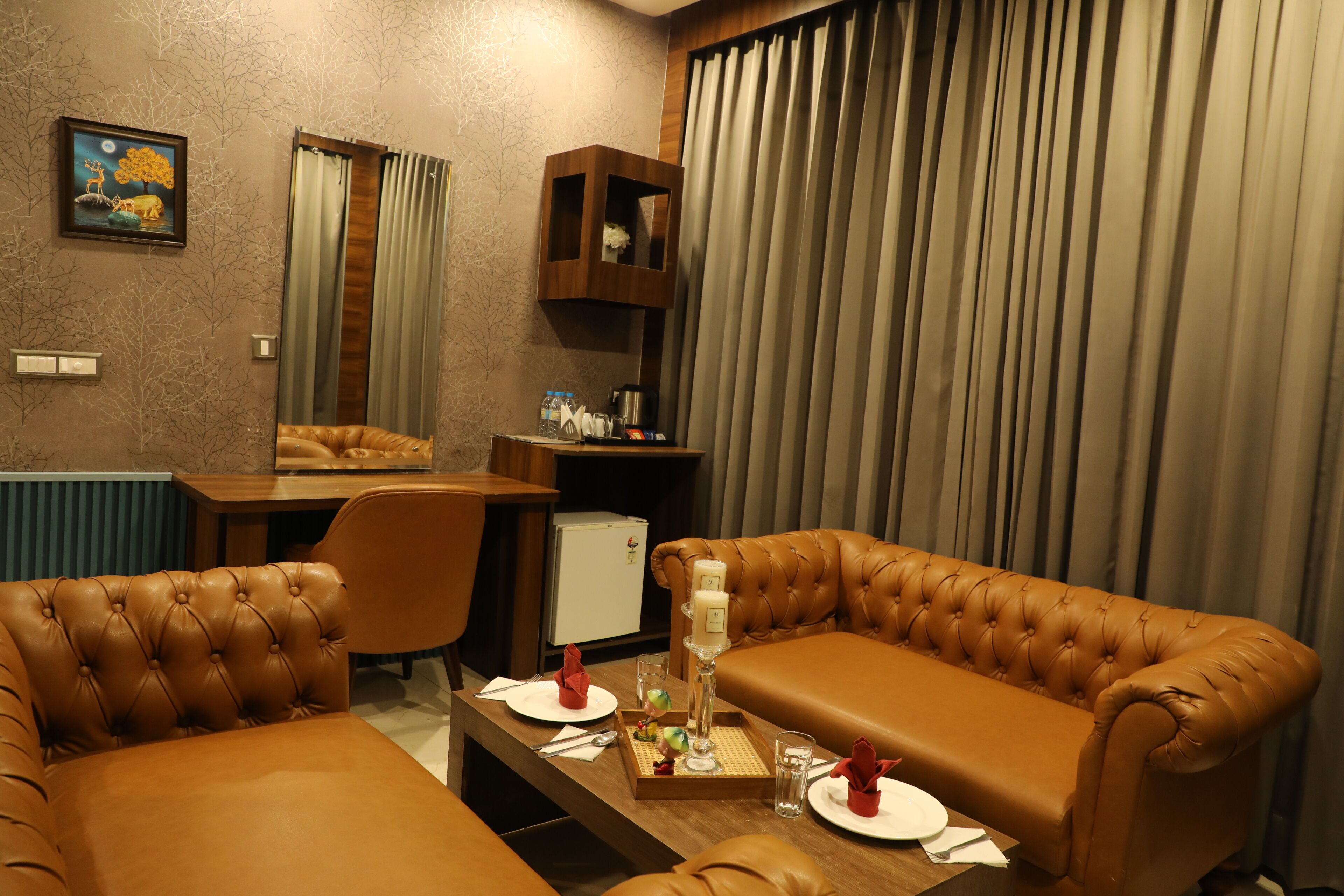 A hotel room with a brown leather sofa set, a small table with a candle, a mirror, and a painting on the wall.