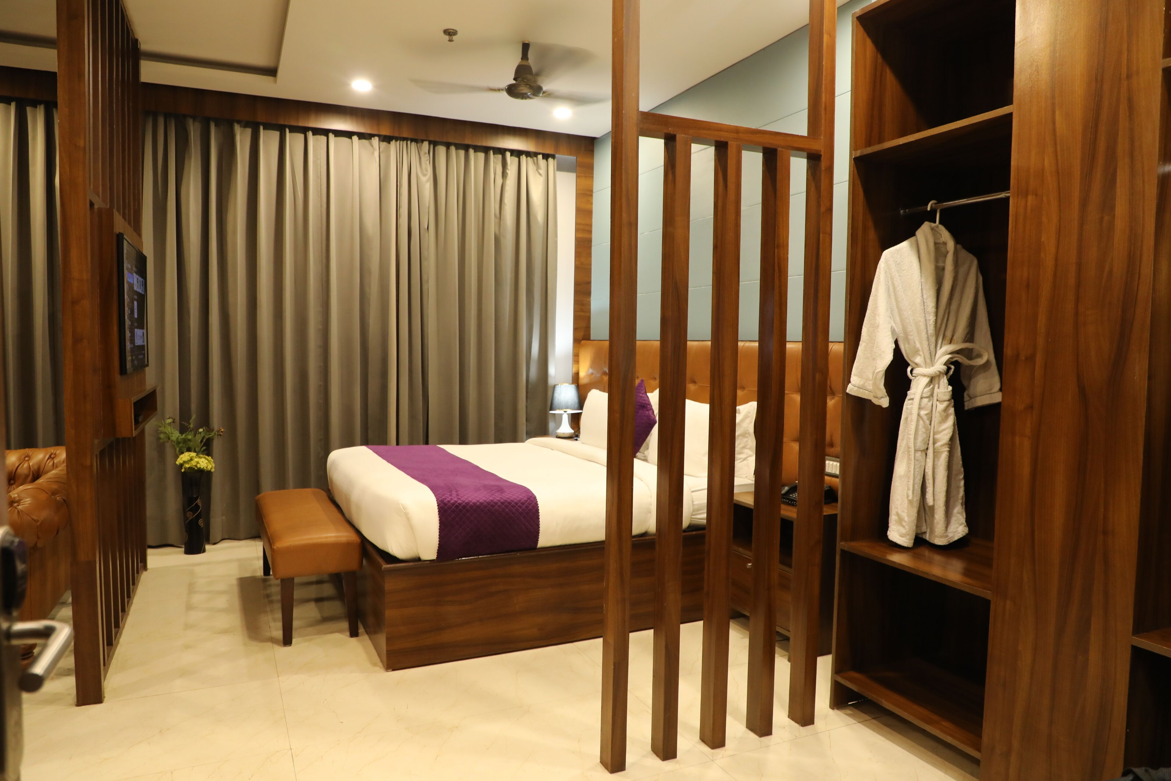 Ein Hotelzimmer mit Bett, Bademantel, Holzschrank, einer Bank und einem kleinen Tisch mit Lampe.