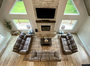 A spacious living room with a stone fireplace, two sofas, a coffee table, and a flat-screen TV mounted above the fireplace. - Wooded Family Escape | Grill | DiscGolf | Big Yard (Plymouth)