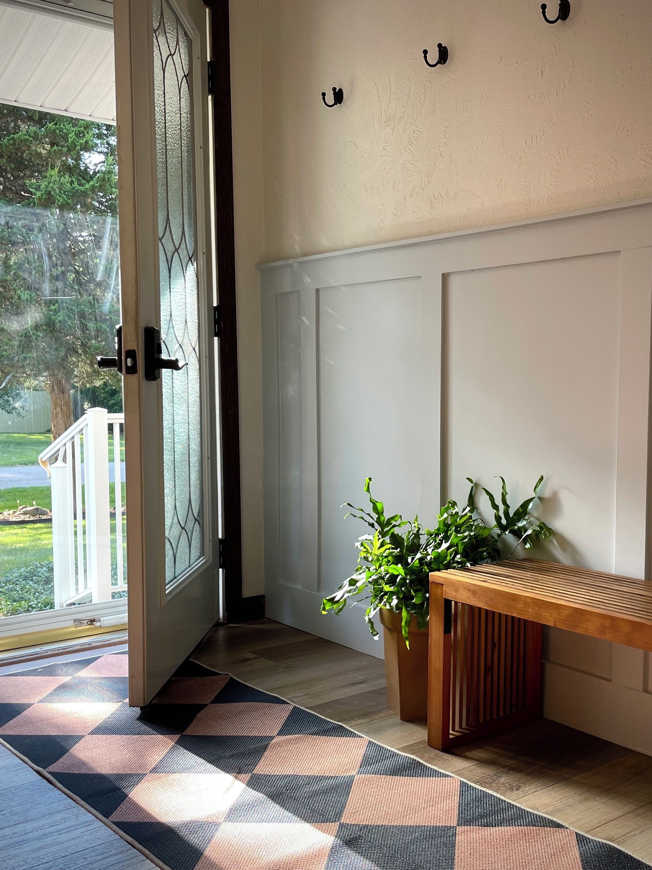 A room with a wooden bench, a potted plant, and a checkered mat on the floor.