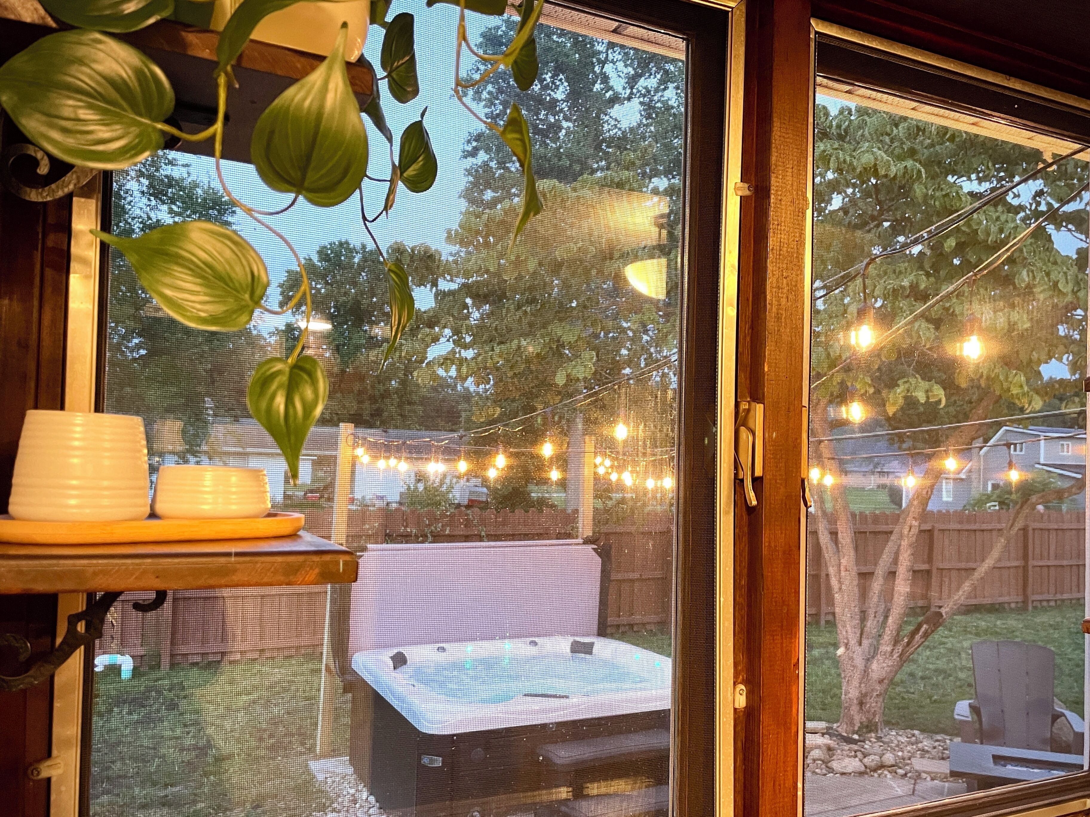 A screened-in patio area with a hot tub, string lights, and a view of the backyard.