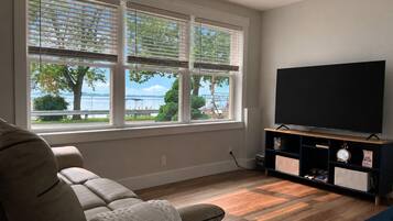 A living room with a large window, a flat-screen TV, a sofa, and a wooden floor.