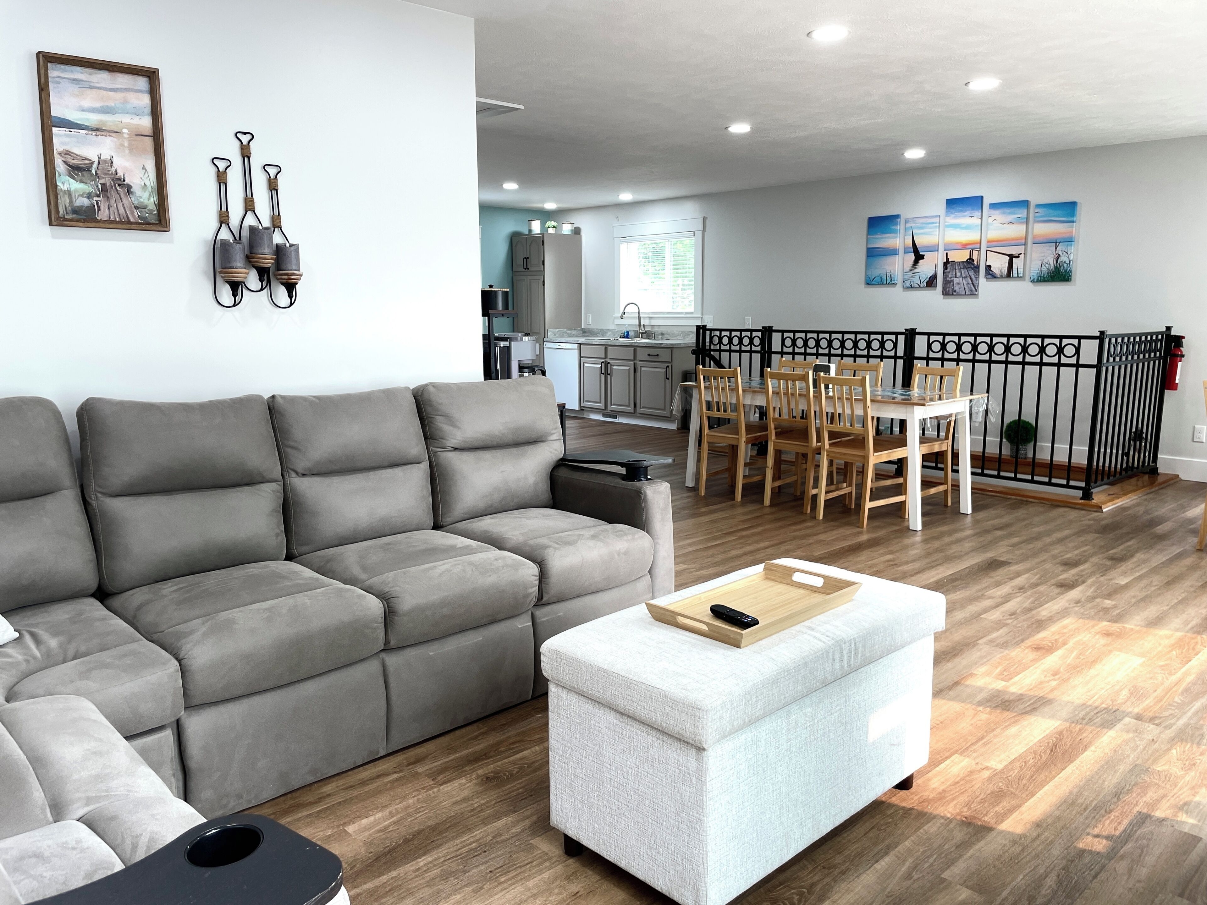 Un salon moderne avec un canapé d’angle gris, un pouf blanc et un coin repas comprenant des chaises et une table en bois.