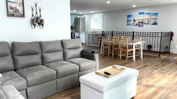 Una sala moderna con un sofá seccional gris, un reposapiés blanco y un comedor con sillas de madera y una mesa.