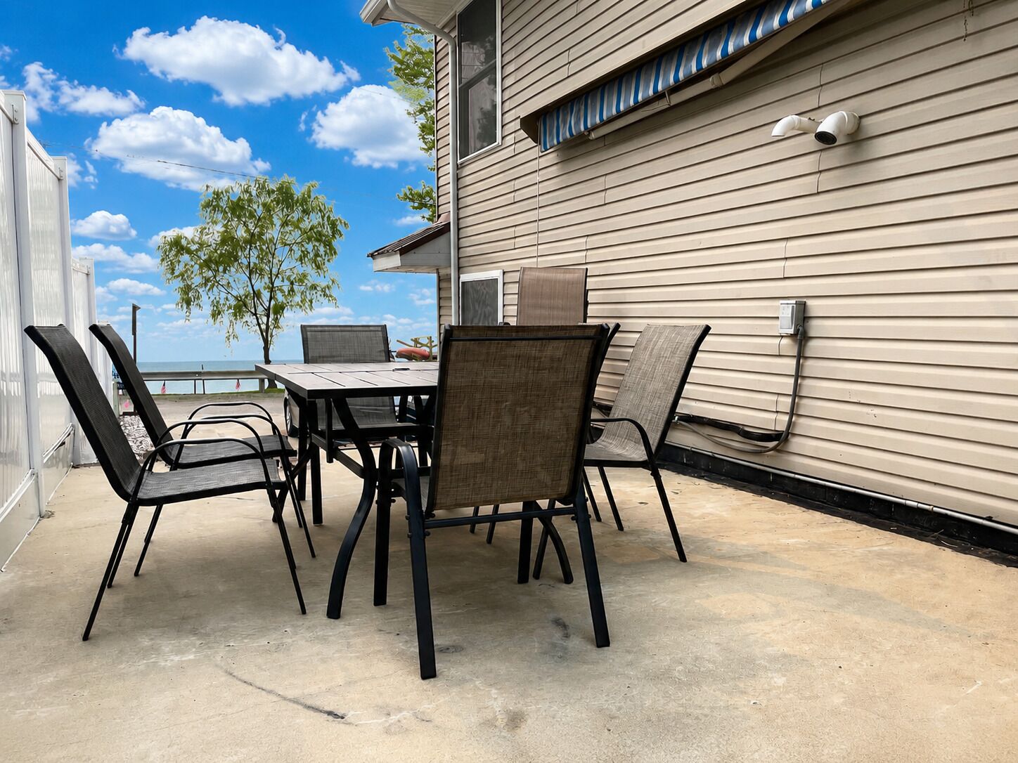 An outdoor patio with a table and chairs, a view of the ocean, and a building with siding and a security camera.